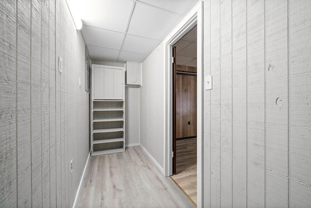 hall featuring a paneled ceiling, baseboards, and light wood finished floors