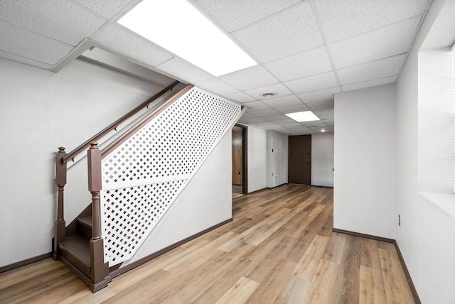 below grade area with a paneled ceiling, wood finished floors, visible vents, baseboards, and stairway