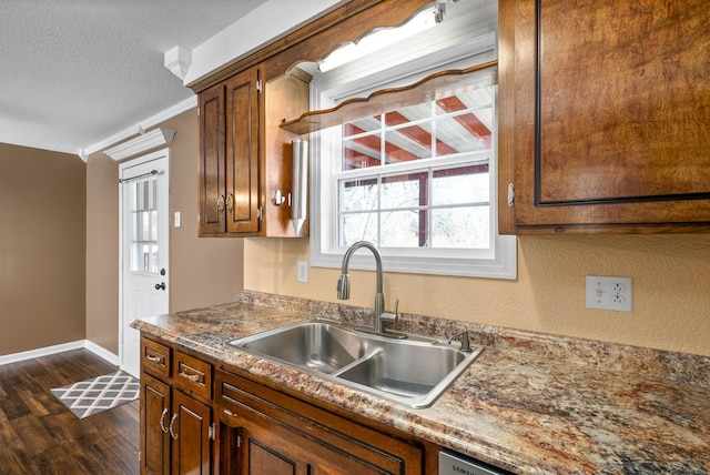 kitchen with dark wood finished floors, ornamental molding, a sink, a textured ceiling, and baseboards