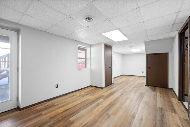 empty room with light wood finished floors, baseboards, visible vents, and a drop ceiling