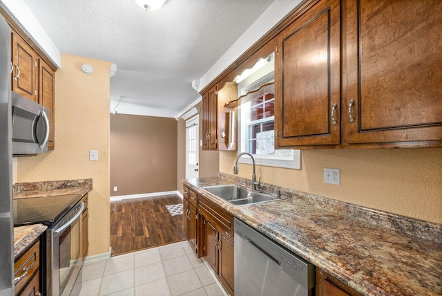 kitchen with light tile patterned floors, a textured ceiling, a textured wall, stainless steel appliances, and a sink