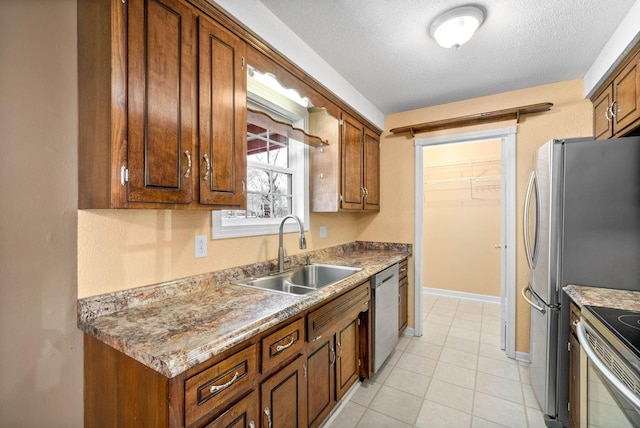 kitchen with baseboards, brown cabinetry, appliances with stainless steel finishes, a textured ceiling, and a sink