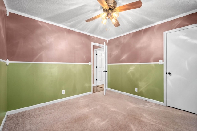 empty room featuring crown molding, carpet flooring, ceiling fan, a textured ceiling, and baseboards