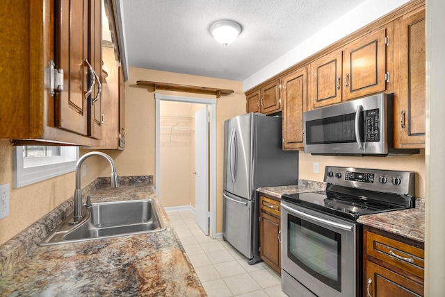 kitchen featuring brown cabinetry, stainless steel appliances, a textured ceiling, a sink, and light tile patterned flooring