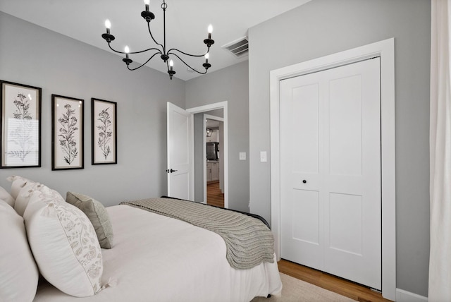 bedroom with visible vents, a closet, a chandelier, and wood finished floors