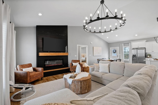 living area featuring light wood finished floors, vaulted ceiling, a large fireplace, and recessed lighting