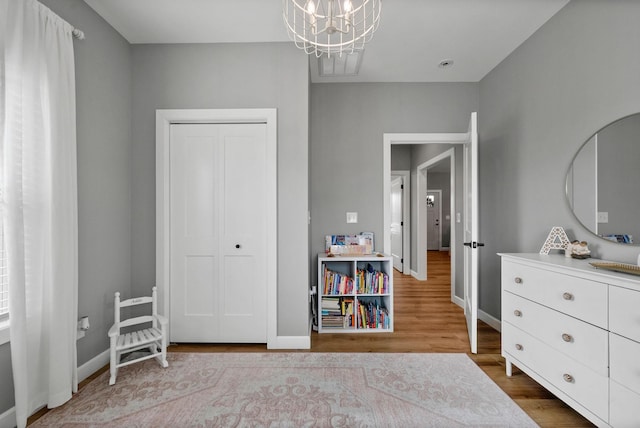 bedroom with a closet, an inviting chandelier, wood finished floors, and baseboards