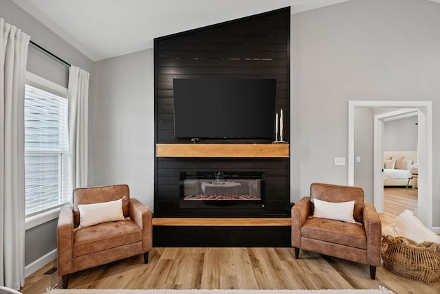 sitting room with vaulted ceiling, a fireplace, and wood finished floors