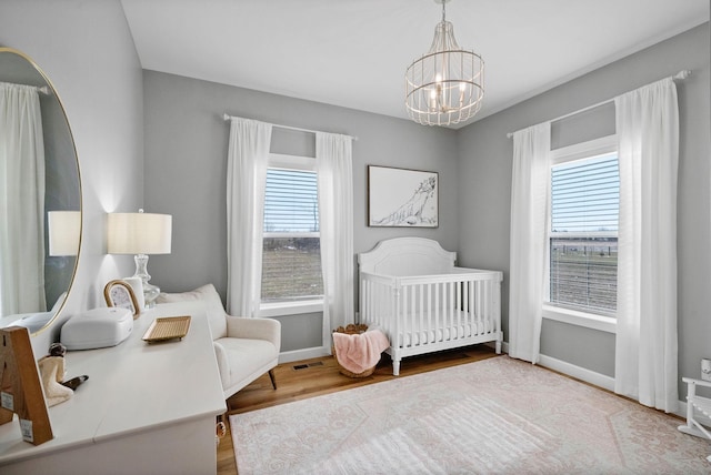 bedroom featuring wood finished floors, multiple windows, a crib, and an inviting chandelier