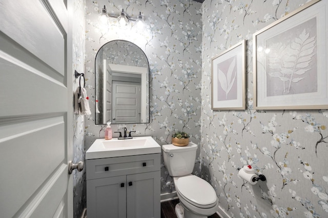 half bath featuring baseboards, vanity, toilet, and wallpapered walls