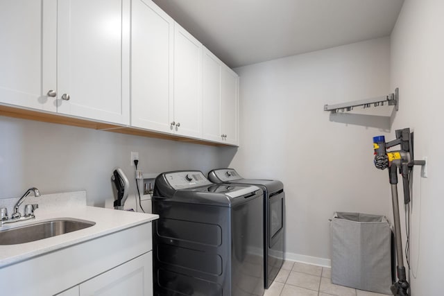 clothes washing area with cabinet space, baseboards, washer and dryer, a sink, and light tile patterned flooring