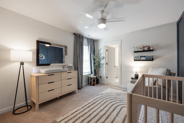 bedroom featuring light carpet, ceiling fan, baseboards, and a crib