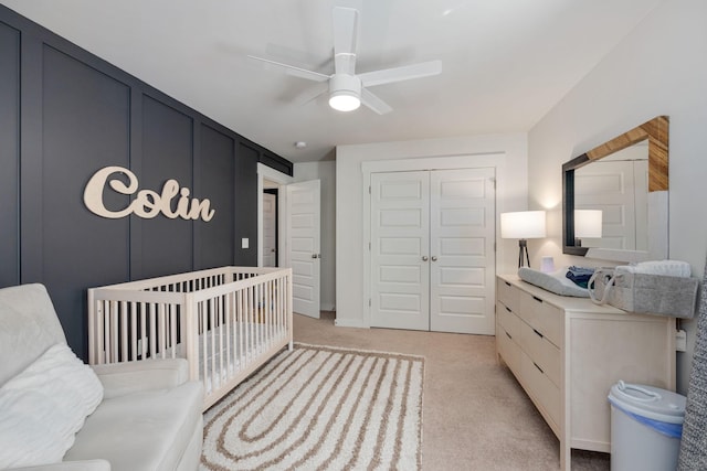 bedroom with light carpet, a nursery area, ceiling fan, and a closet