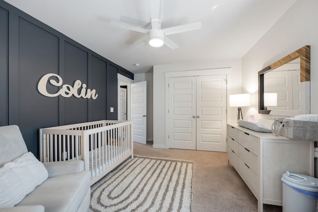 bedroom featuring light carpet, ceiling fan, a closet, and a decorative wall