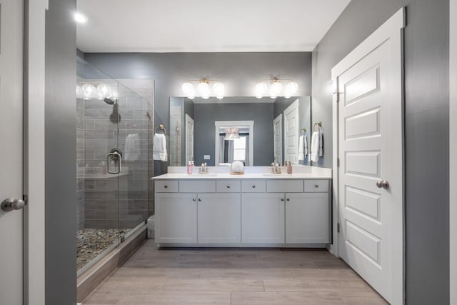 full bathroom featuring double vanity, a stall shower, a sink, and wood finished floors