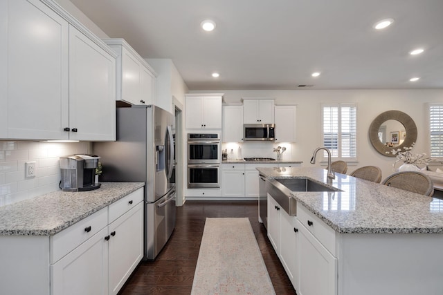 kitchen with white cabinets, a center island with sink, stainless steel appliances, and a sink