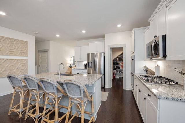 kitchen with light stone counters, dark wood-style flooring, a sink, appliances with stainless steel finishes, and decorative backsplash