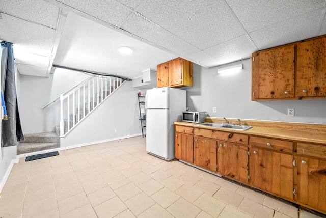 kitchen featuring a sink, light countertops, freestanding refrigerator, brown cabinets, and stainless steel microwave