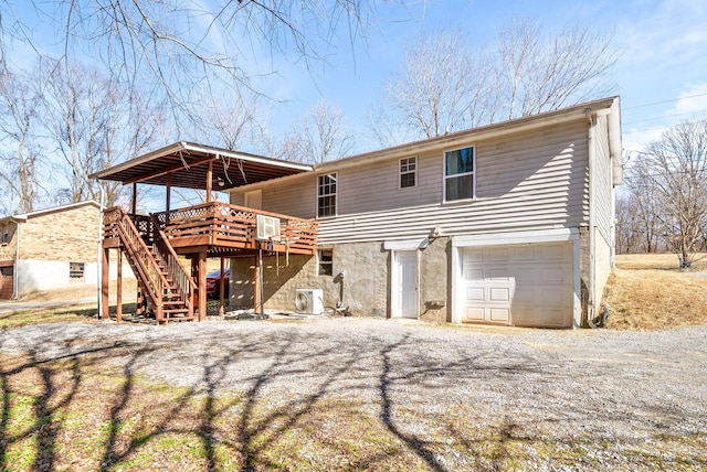 rear view of property featuring an attached garage, stairway, a wooden deck, ac unit, and gravel driveway