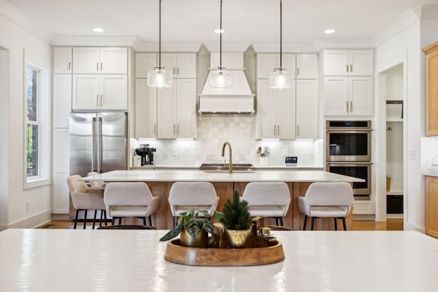 kitchen with stainless steel appliances, light countertops, custom range hood, and a kitchen breakfast bar