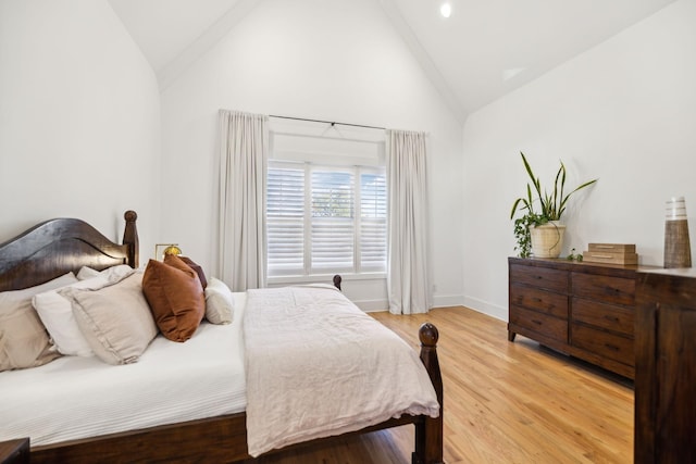 bedroom featuring light wood finished floors, baseboards, and high vaulted ceiling