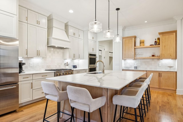 kitchen with an island with sink, appliances with stainless steel finishes, light wood-style floors, premium range hood, and open shelves