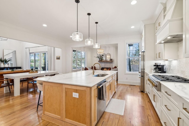 kitchen featuring a kitchen island with sink, a sink, appliances with stainless steel finishes, tasteful backsplash, and custom range hood