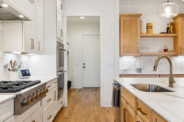 kitchen with a sink, appliances with stainless steel finishes, custom exhaust hood, light stone countertops, and light wood finished floors