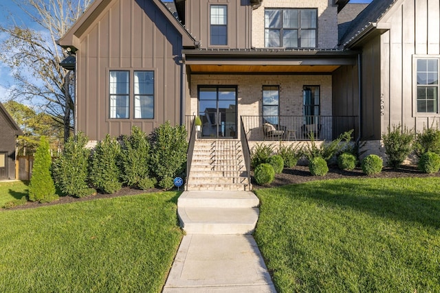 entrance to property with board and batten siding, brick siding, a yard, and a porch