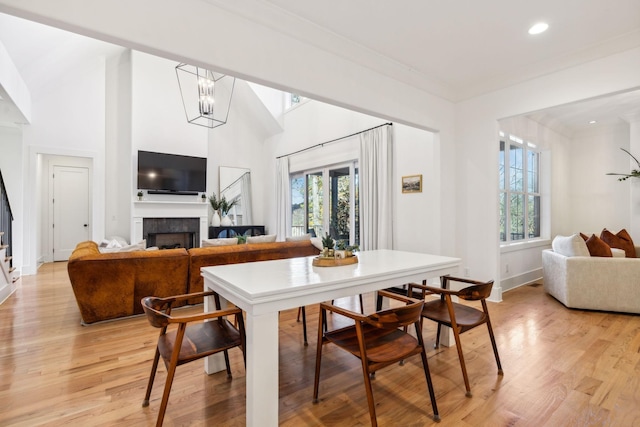 dining area with a notable chandelier, a fireplace, crown molding, recessed lighting, and light wood-style floors