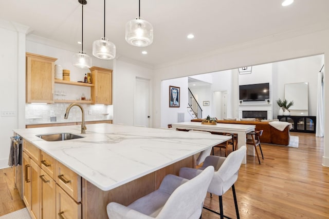 kitchen featuring a kitchen island with sink, a fireplace, a sink, light wood-type flooring, and crown molding