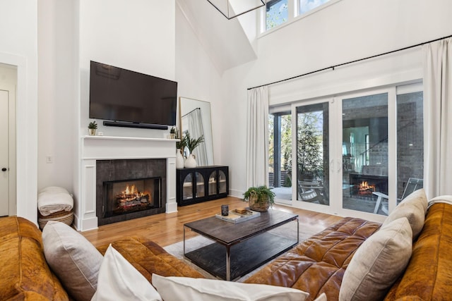 living area with a lit fireplace, wood finished floors, and a towering ceiling