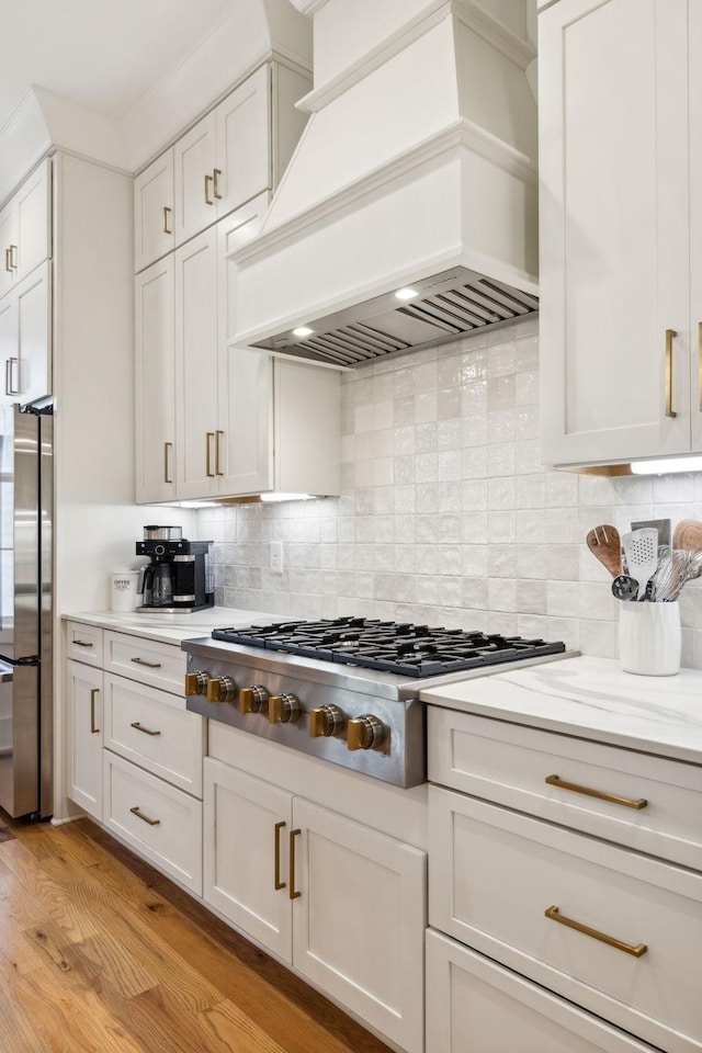 kitchen with white cabinetry, appliances with stainless steel finishes, light wood-type flooring, tasteful backsplash, and custom range hood