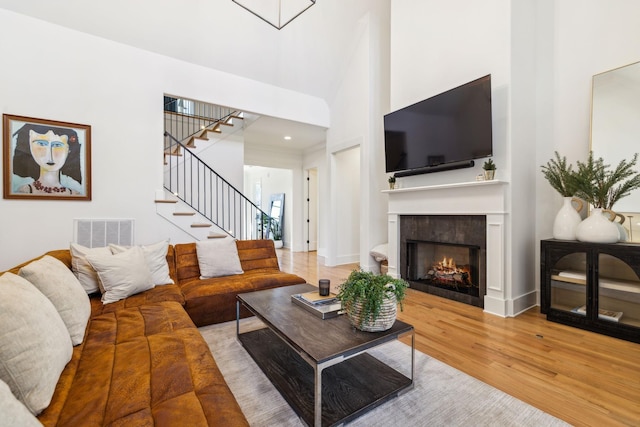 living area with visible vents, stairway, a high ceiling, a tiled fireplace, and wood finished floors