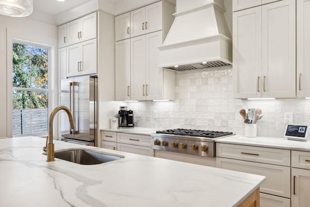 kitchen with stainless steel appliances, tasteful backsplash, white cabinets, a sink, and premium range hood