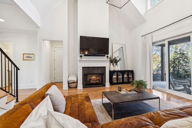 living room featuring wood finished floors, a towering ceiling, baseboards, stairway, and a tiled fireplace