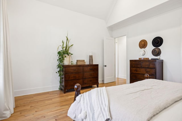 bedroom featuring light wood-style floors, lofted ceiling, and baseboards