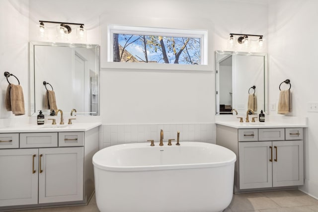 bathroom with tile walls, a soaking tub, two vanities, wainscoting, and a sink