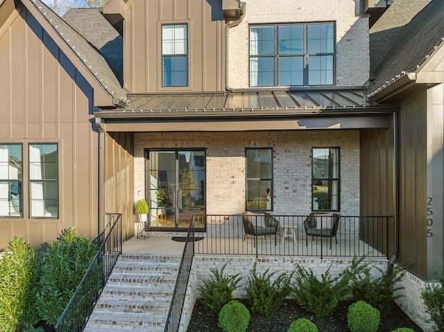 view of exterior entry with brick siding, covered porch, board and batten siding, a standing seam roof, and metal roof