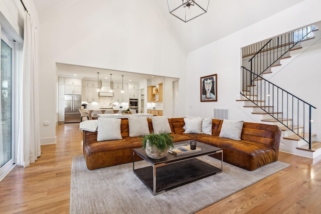 living room featuring light wood finished floors, visible vents, high vaulted ceiling, baseboards, and stairs