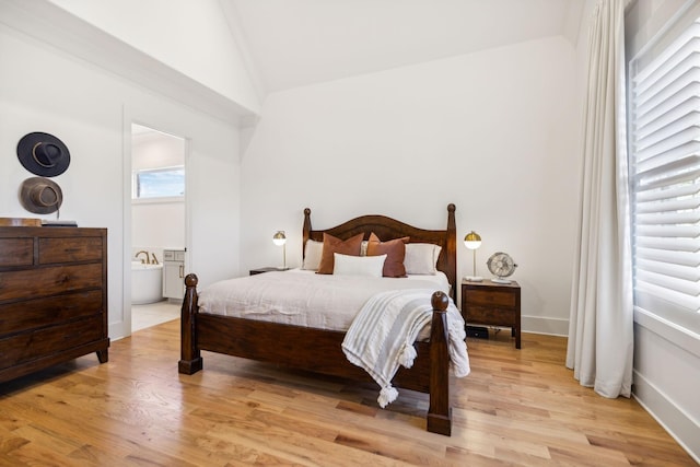 bedroom with lofted ceiling, baseboards, light wood-style flooring, and ensuite bath