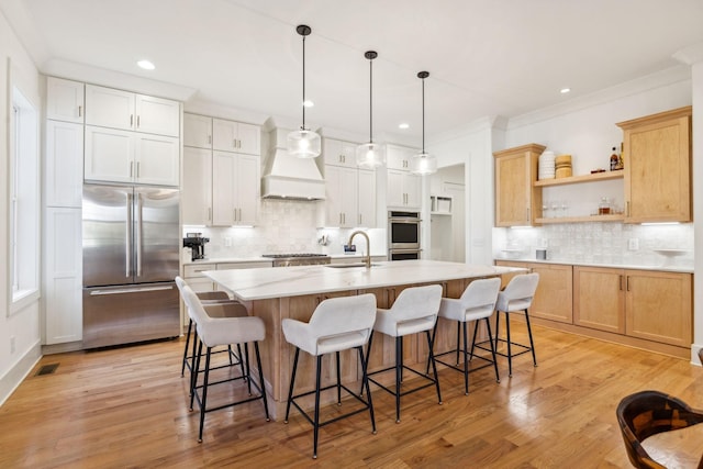 kitchen with custom exhaust hood, stainless steel appliances, light countertops, open shelves, and a sink