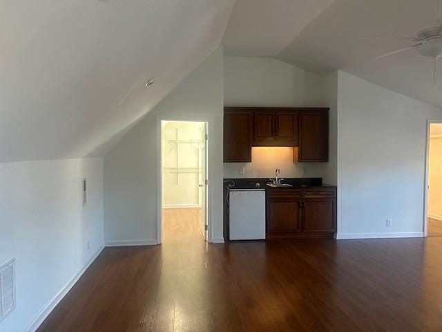 kitchen featuring dark countertops, dark wood-type flooring, white dishwasher, and baseboards