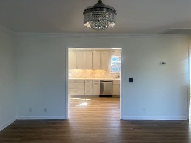 unfurnished dining area featuring an inviting chandelier, crown molding, baseboards, and wood finished floors