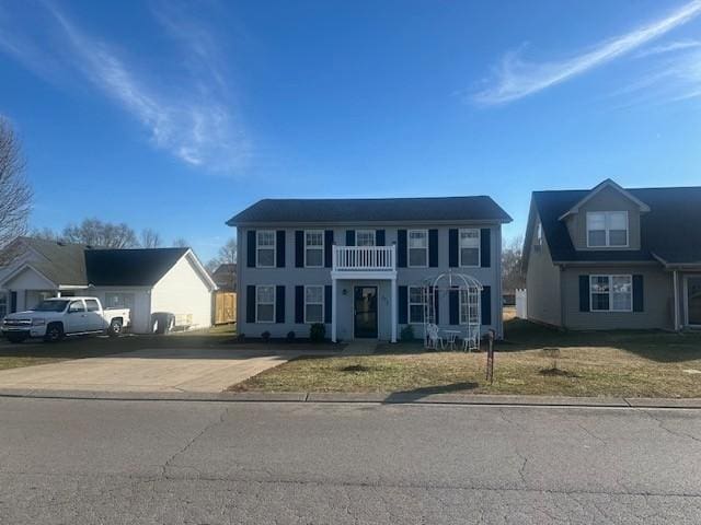 colonial home with driveway, a front yard, and a balcony