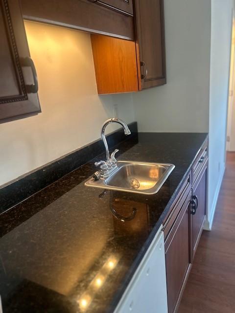 kitchen with dark wood-type flooring, white dishwasher, a sink, and baseboards