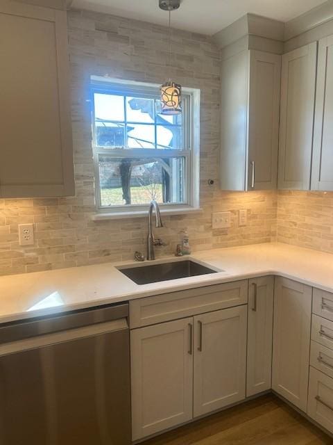 kitchen featuring decorative light fixtures, light countertops, backsplash, a sink, and dishwasher