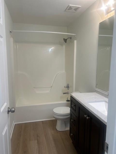 bathroom featuring visible vents, toilet, wood finished floors, tub / shower combination, and vanity