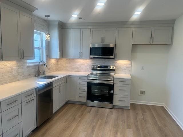 kitchen with light countertops, light wood-style flooring, appliances with stainless steel finishes, a sink, and baseboards