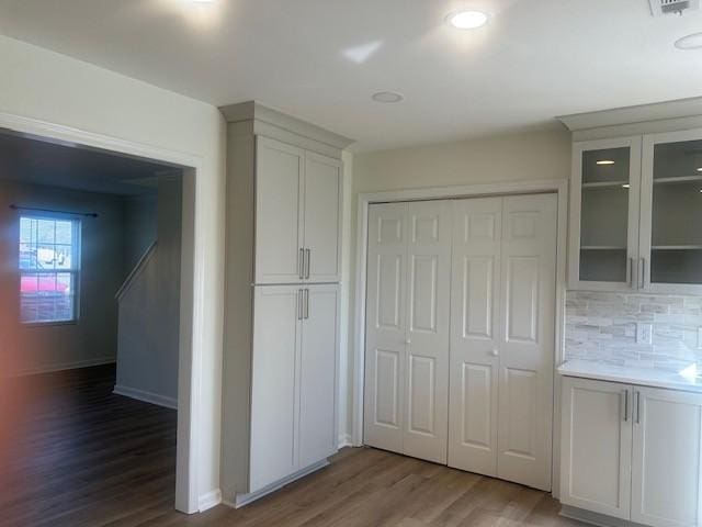 interior space featuring tasteful backsplash, baseboards, glass insert cabinets, wood finished floors, and light countertops